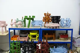 Bunte Keramikskulpturen auf blauen Metallregalen ausgestellt.