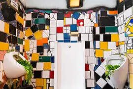 Toaletă publică cu design artistic, decorată cu mozaicuri colorate și forme organice inspirate de Hundertwasser.