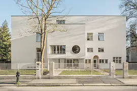 Vue sur rue de la villa moderniste avec fenêtre ronde et entrée en retrait.