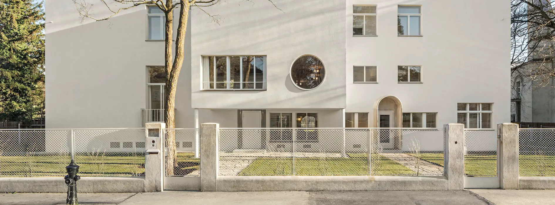 Vue sur rue de la villa moderniste avec fenêtre ronde et entrée en retrait.