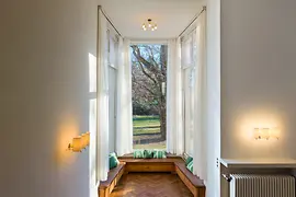 Intérieur lumineux avec de grandes fenêtres, des banquettes encastrées et une vue sur la verdure.