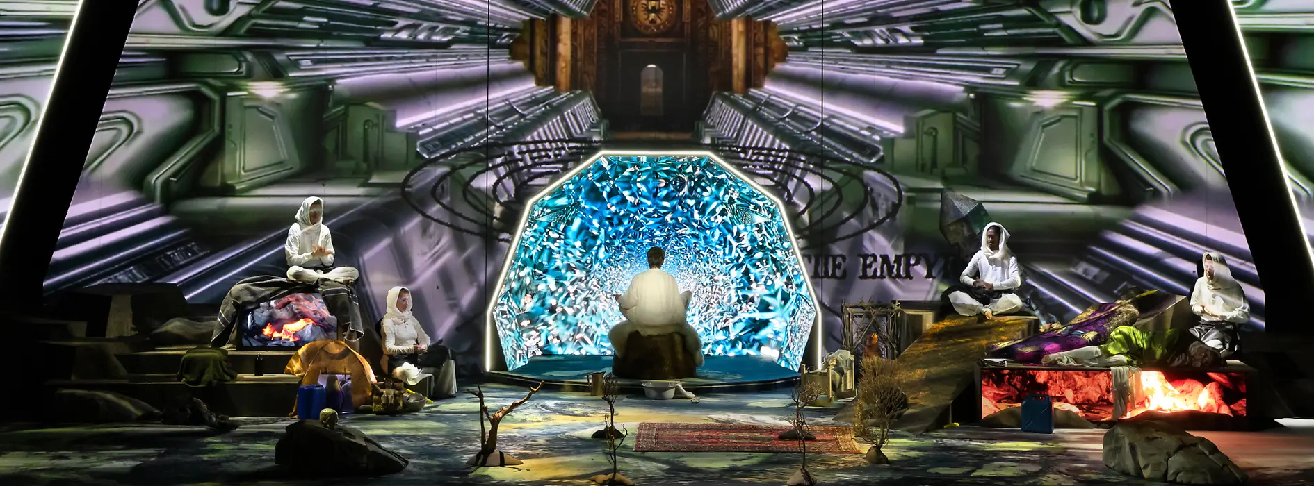 Futuristic stage installation with several performers in front of a glowing digital backdrop.