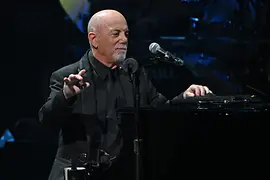 Billy Joel leaning on the piano, the microphone in front of him.