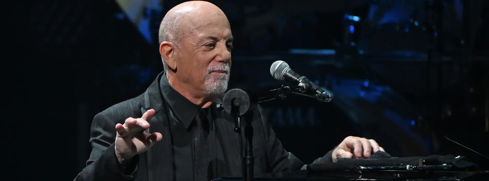 Billy Joel leaning on the piano, the microphone in front of him.