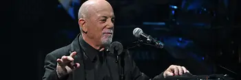 Billy Joel appoggiato al pianoforte, davanti a sé il microfono.