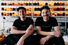 Two men sitting in front of large preserving jars