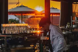 Hote Motto Rooftop-Bar Chez Bernard, Barkeeper mischt Getränke, Sonnenuntergang im Hintergrund