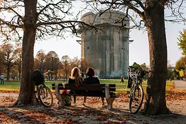 Dwie osoby siedzą na ławce z widokiem na wieżę przeciwlotniczą w Augarten